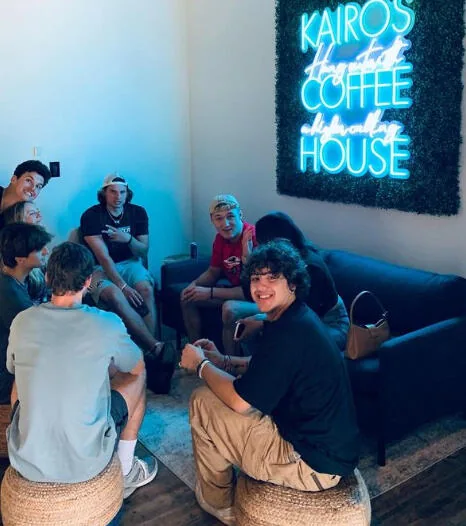 Friends on the couch beneath the Kairos Coffee House neon sign